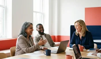 Drie diverse professionals in gesprek aan een moderne werktafel in een lichte kantoorruimte met natuurlijk daglicht.