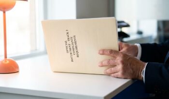Professional hands holding Track 2 compliance government document on white desk with natural lighting